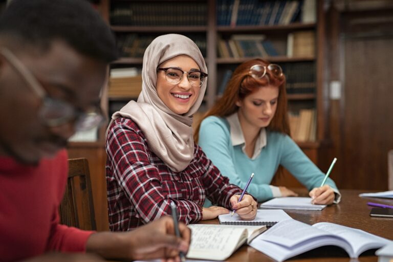 Jeune étudiante en hijab souriant et travaillant avec d'autres étudiants.