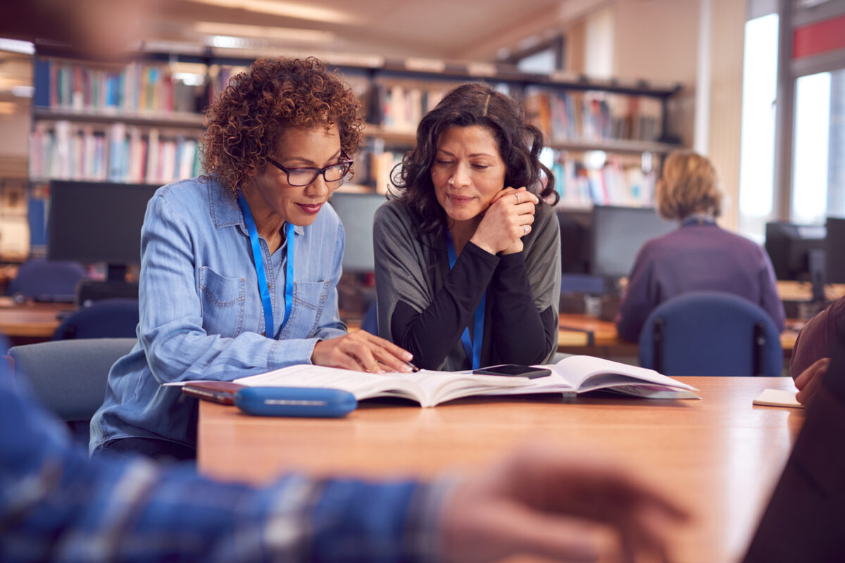 Professionnel du soutien scolaire avec Étudiante adulte femme mûre assise à une table travaillant dans la bibliothèque d'un collège