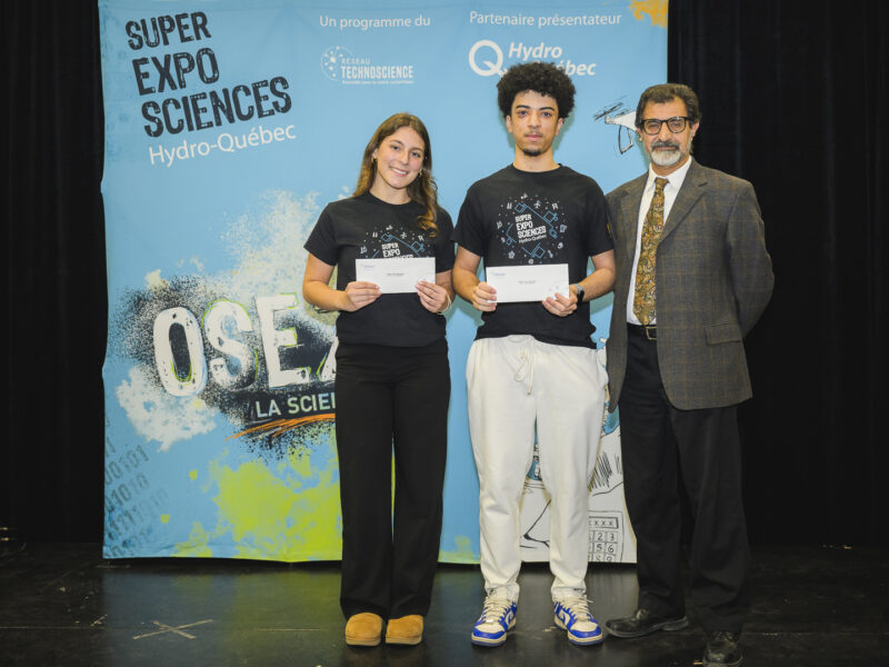 Un étudiant et une étudiante se tenant côte à côte à côté d'un fonctionnaire et tenant leur prix du concours de sciences.