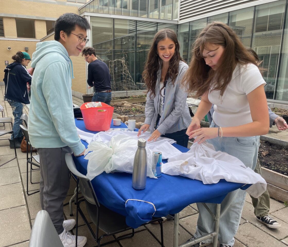 trois étudiants à une table de travail en plein air se préparant à teindre leurs blouses à la cravate 