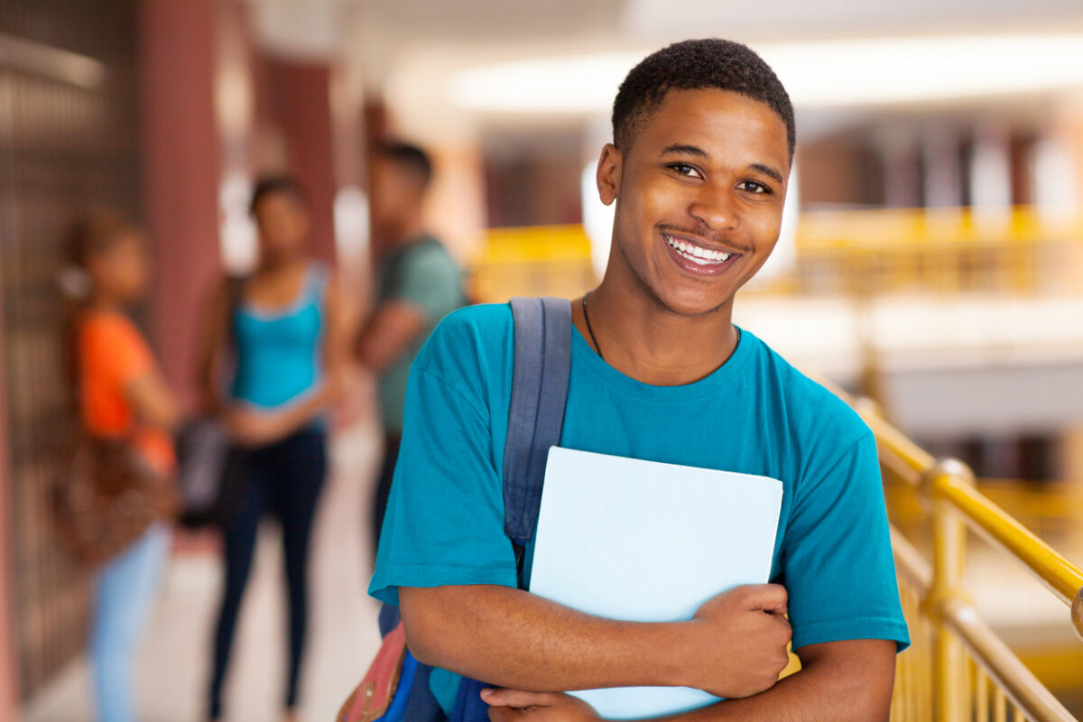 smiling college student holding books against his chest 