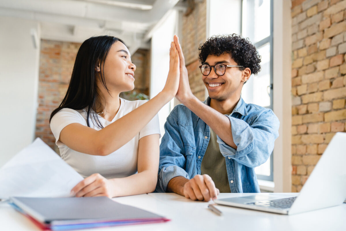 deux étudiants souriants se congratulent devant leur ordinateur portable