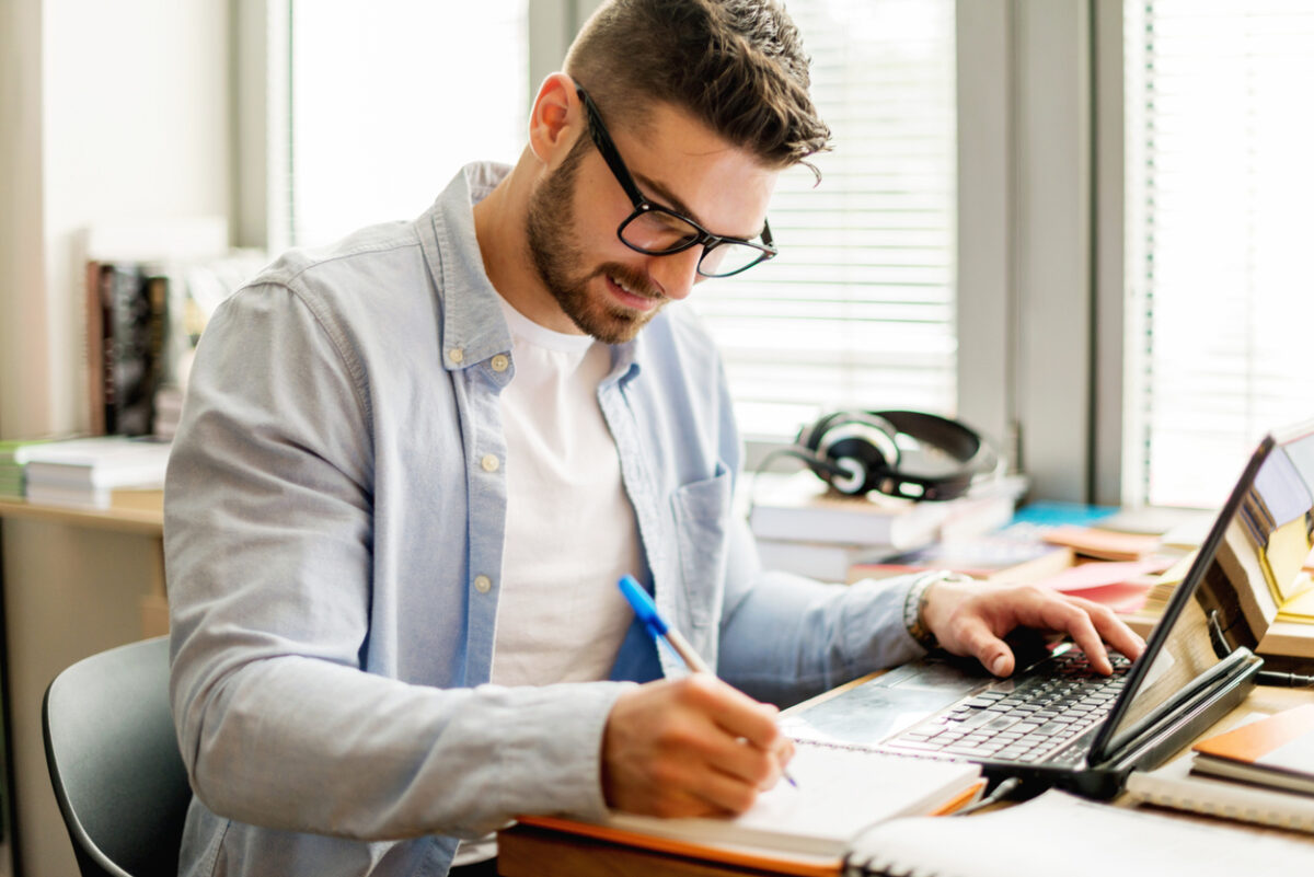 a male student looking at a laptop and taking notes
