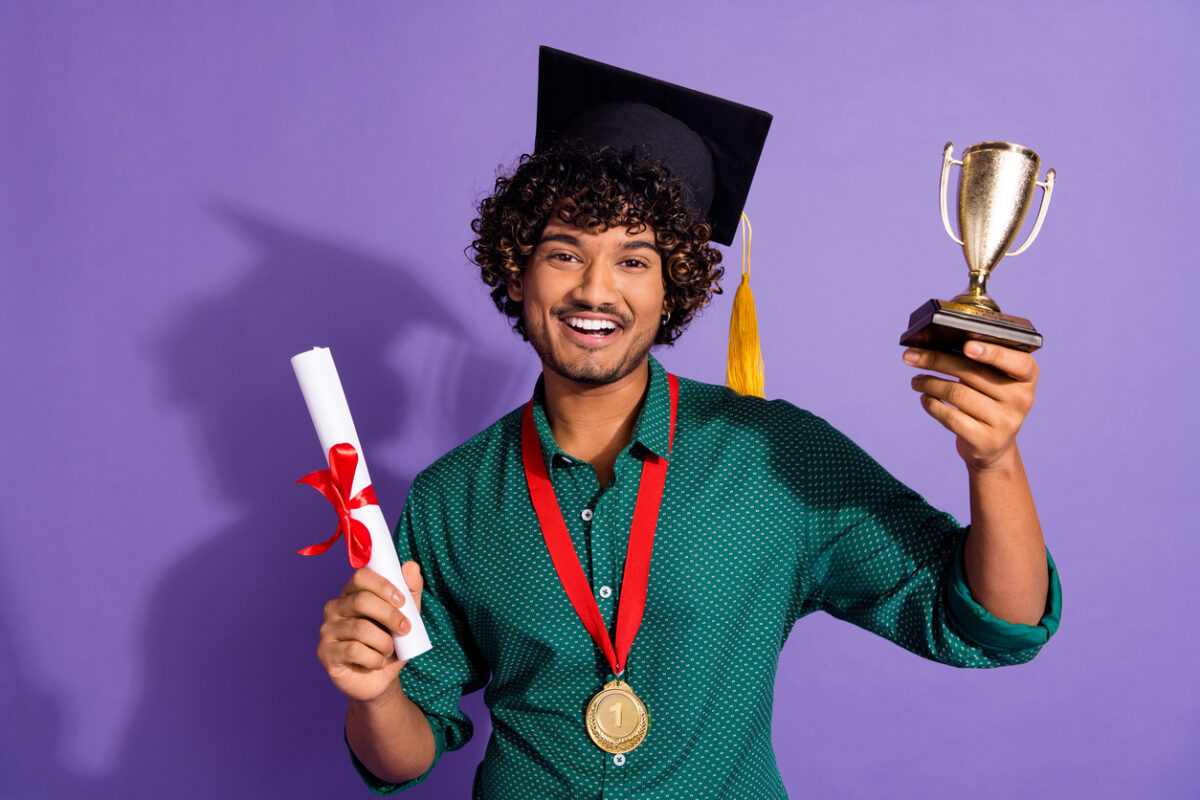 student wearing graduation cap and holding certificate and trophy