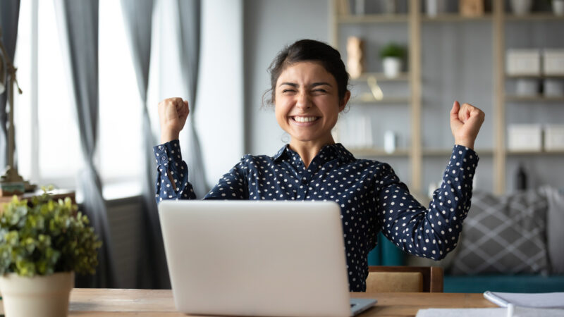 smiling student with arms raised in victory looking at test results on her laptop