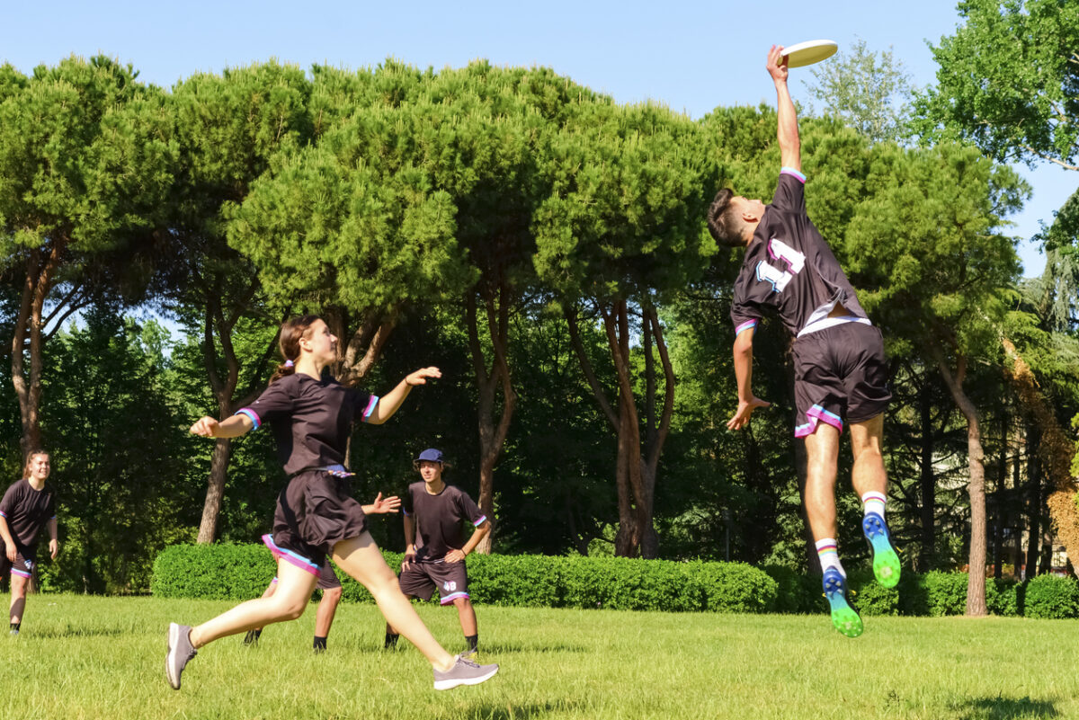 un groupe de jeunes adultes en tenue d'équipe jouant à l'ultimate frisbee sur un terrain ensoleillé