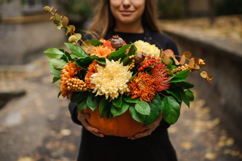 Femme tenant une citrouille avec des fleurs d'automne